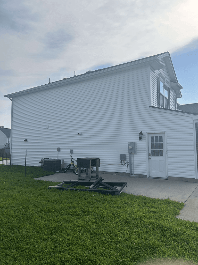 Side elevation showing completed white siding with coordinated soffit, gutters, downspouts, and roof edge