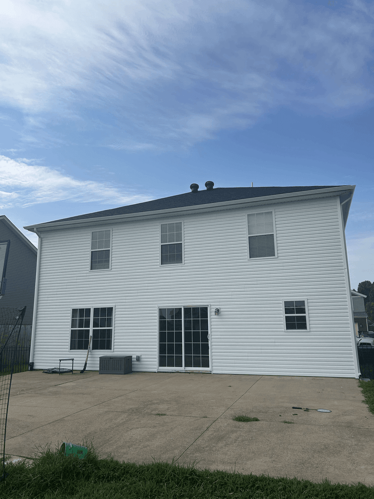 Rear view of a two-story home with completed white siding, dark roofing, gutters, and downspouts