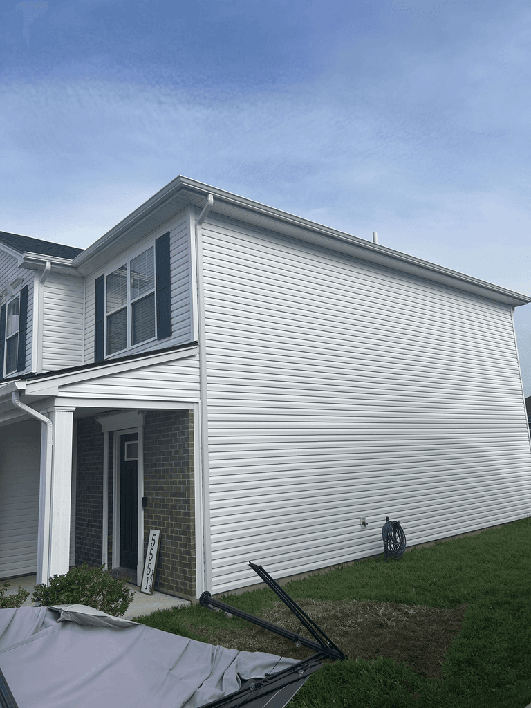 Front-side view highlighting white siding, soffit, gutters, downspout, and the finished roofline