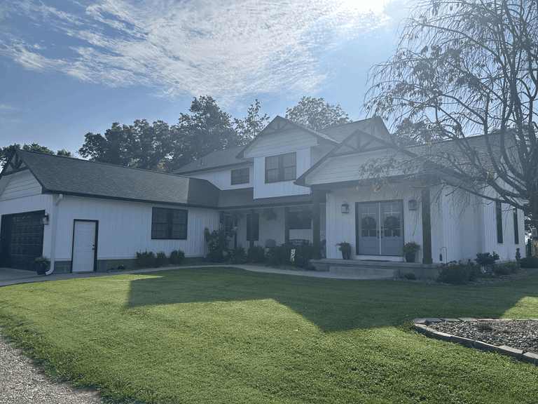 Wide view of a completed white farmhouse exterior with coordinated siding, dark roofing, fascia, soffit, and gutters