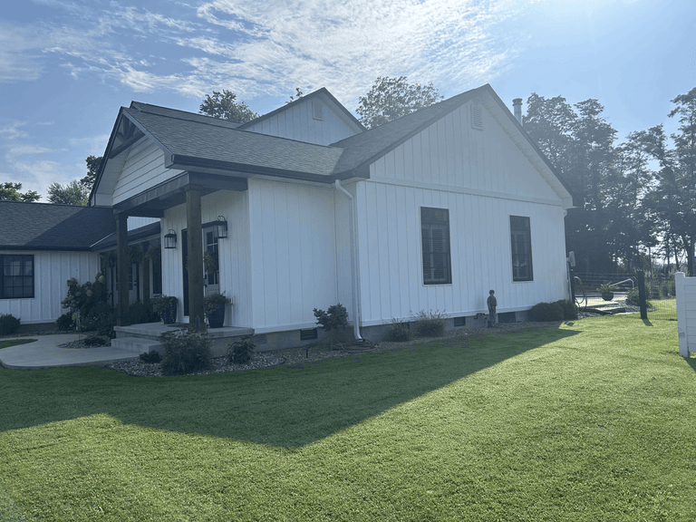 Side view of white board-and-batten siding with dark roofing, fascia, soffit, gutters, and downspouts