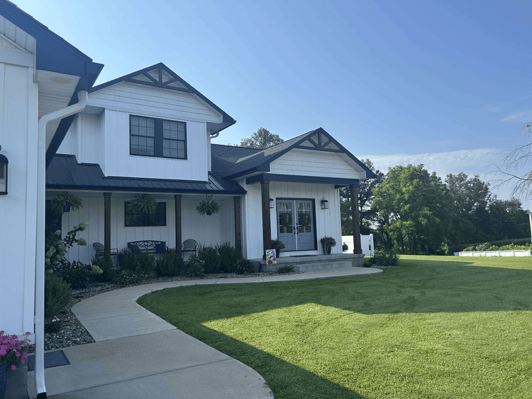 Front entry of a white farmhouse exterior with board-and-batten siding, shingle accents, dark roofing, fascia, soffit, and gutters