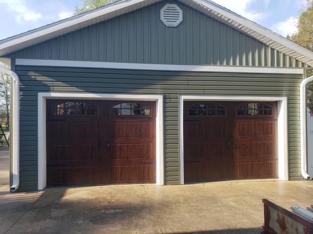 Detached garage with two finished wood-look overhead doors and new siding